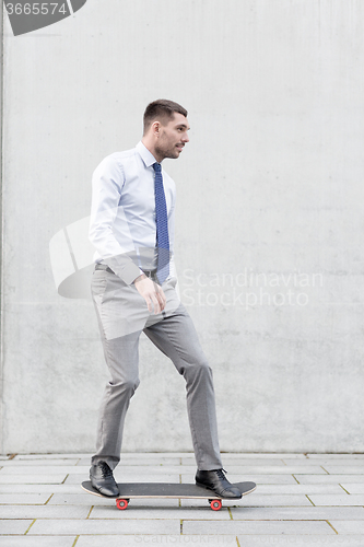 Image of young smiling businessman with skateboard outdoors