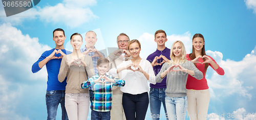 Image of people showing heart hand sign over sky and clouds