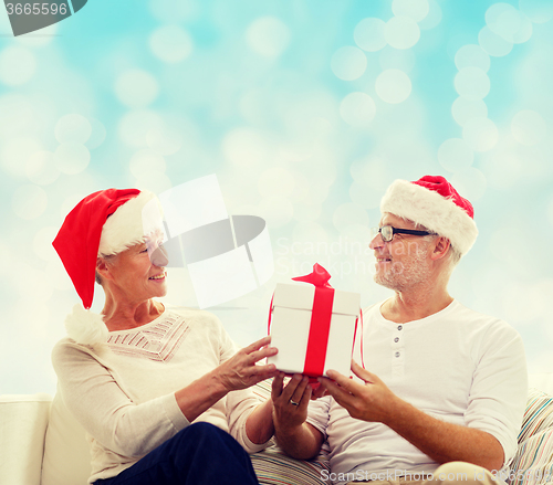 Image of happy senior couple in santa hats with gift box