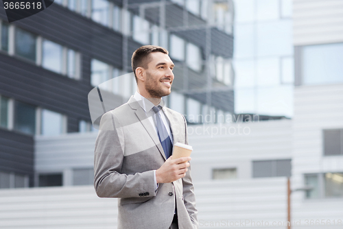 Image of young serious businessman with paper cup outdoors