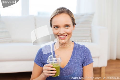 Image of happy woman with smoothie sitting on mat at home