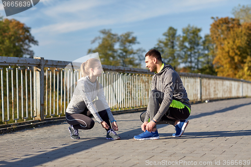 Image of smiling couple tying shoelaces outdoors