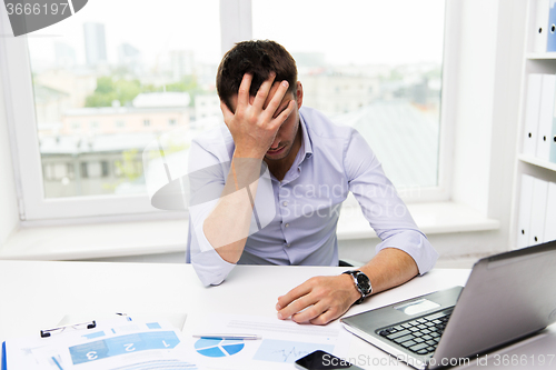 Image of businessman with laptop and papers in office