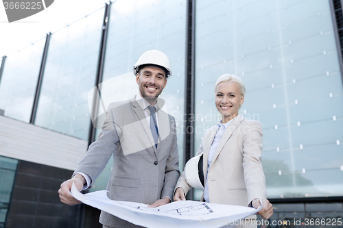 Image of smiling businessmen with blueprint and helmets