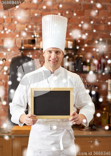 Image of happy male chef with blank menu board in kitchen