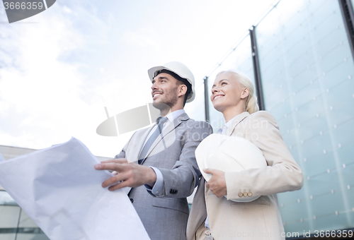 Image of smiling businessmen with blueprint and helmets