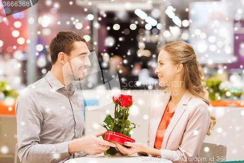 Image of happy couple with present and flowers in mall