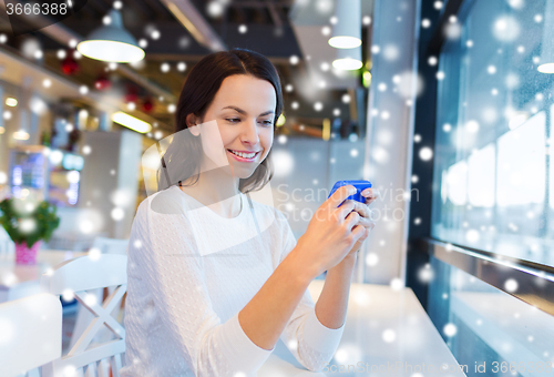 Image of smiling woman with smartphone at cafe