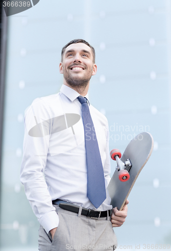 Image of young smiling businessman with skateboard outdoors