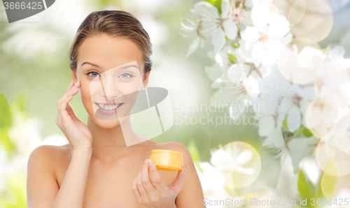 Image of happy young woman applying cream to her face