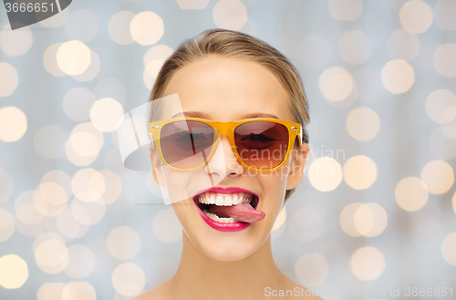 Image of happy young woman in sunglasses showing tongue