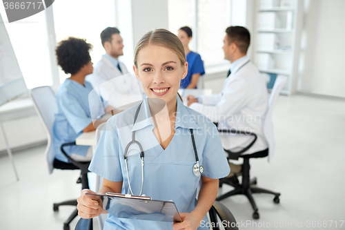 Image of happy doctor with clipboard over group of medics