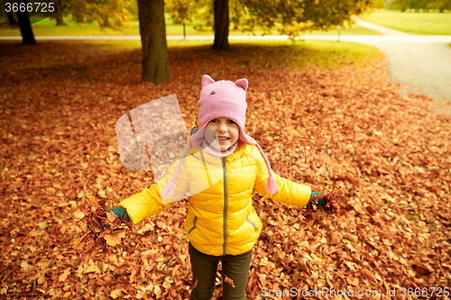 Image of happy girl playing with autumn leaves in park