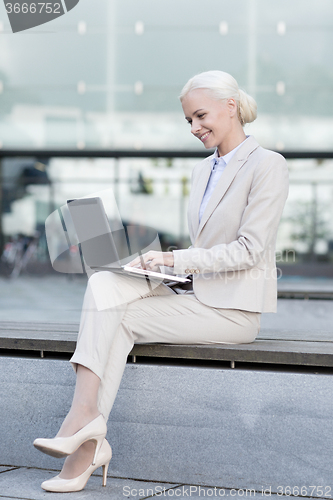 Image of smiling businesswoman working with laptop outdoors