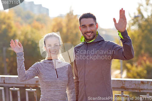 Image of smiling couple waving hand outdoors