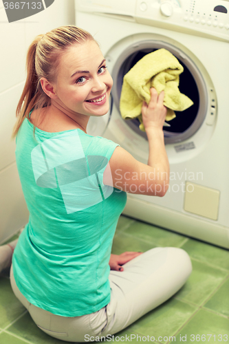 Image of happy woman putting laundry into washer at home