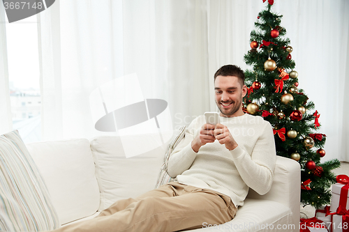 Image of smiling man with smartphone at home for christmas