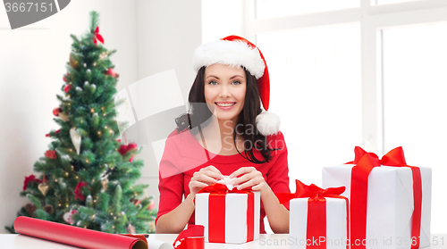 Image of smiling woman in santa helper hat packing gifts