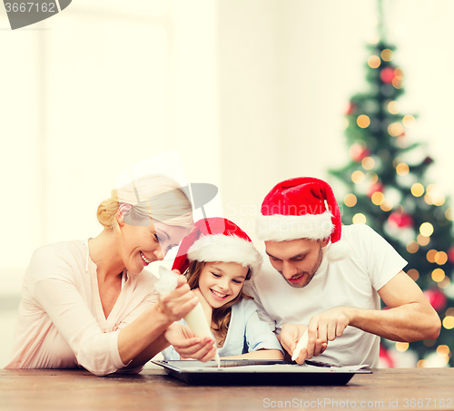 Image of happy family in santa helper hats making cookies