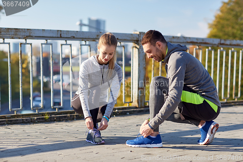 Image of smiling couple tying shoelaces outdoors