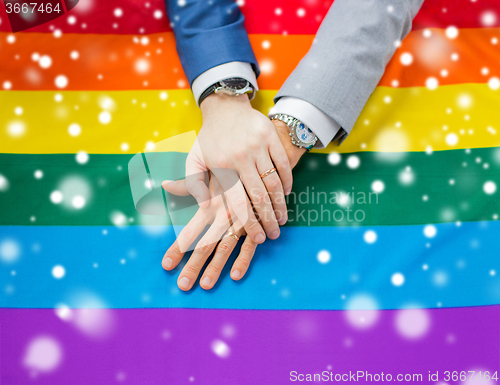 Image of close up of male gay couple hands on rainbow flag