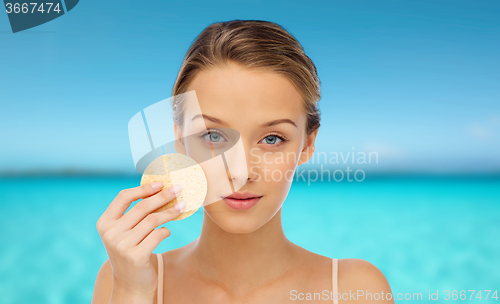 Image of young woman cleaning face with exfoliating sponge