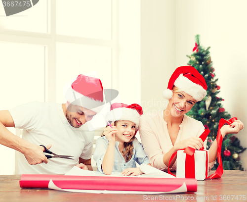 Image of happy family in santa helper hats packing gift