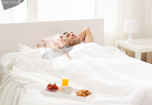 Image of happy couple lying in bed with tray of breakfast