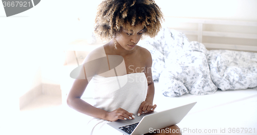 Image of Happy woman using laptop on bed.