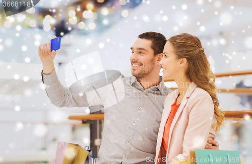 Image of happy couple with smartphone taking selfie in mall