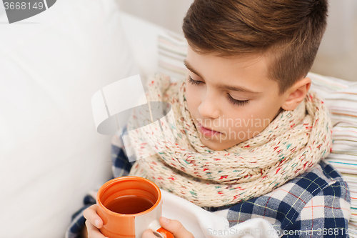 Image of ill boy with flu in scarf drinking tea at home