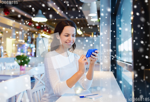 Image of smiling woman with smartphone at cafe