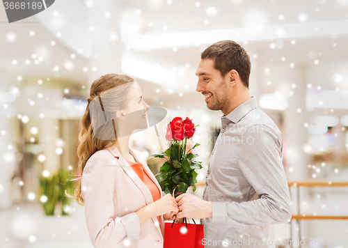 Image of man giving woman red roses and present in mall