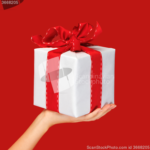 Image of close up hand holding christmas gift box over red