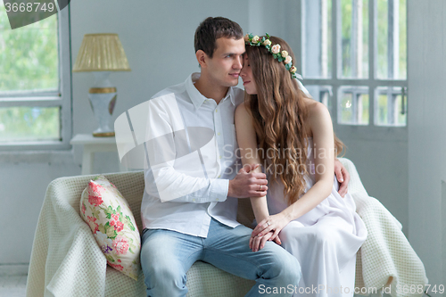 Image of Cheerful young couple  dressed in white sitting on sofa 