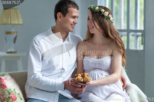Image of Cheerful young couple with baby shoes sitting at home