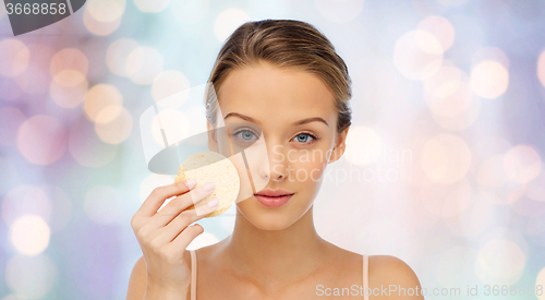 Image of young woman cleaning face with exfoliating sponge