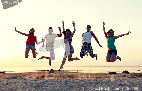 Image of smiling friends dancing and jumping on beach