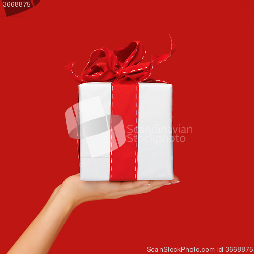 Image of close up hand holding christmas gift box over red