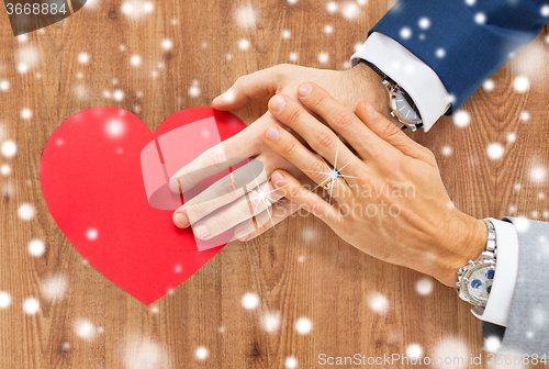 Image of close up of male gay couple hands with red heart