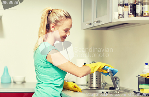 Image of happy woman cleaning tap at home kitchen