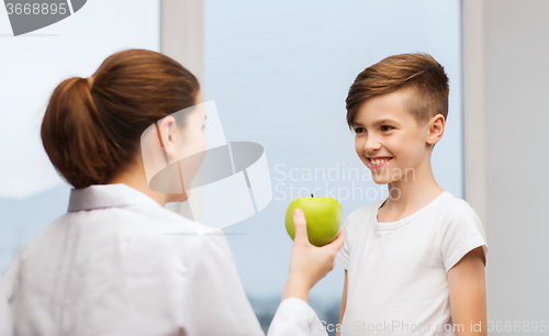 Image of doctor with green apple and happy boy in clinic