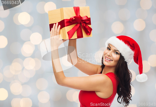 Image of beautiful woman in santa hat with gift over lights