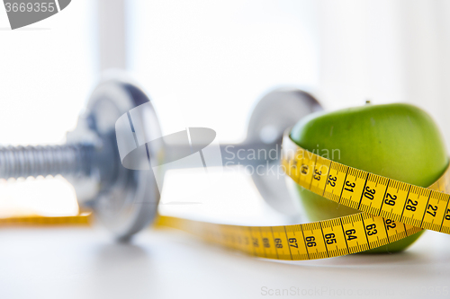 Image of close up of dumbbell and apple with measuring tape