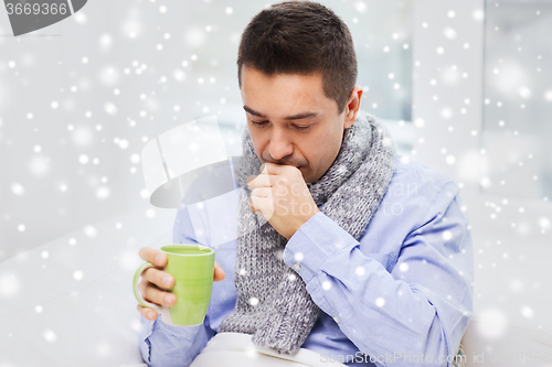 Image of ill man with flu drinking tea and coughing at home