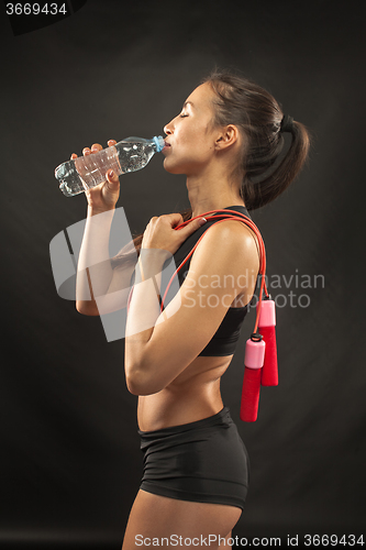 Image of Muscular young woman athlete with a skipping rope on black 