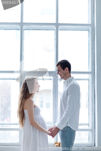 Image of Cheerful young couple  dressed in white sitting on sofa 
