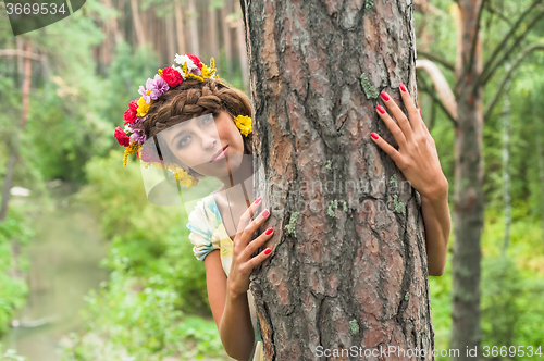 Image of Attractive woman with flower wreath behind pine