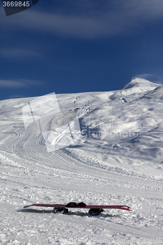 Image of Snowboard in snow on ski slope at sun windy day