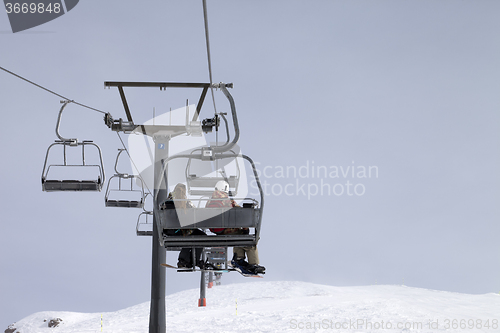 Image of Snowboarders on chair-lift and ski slope at gray day